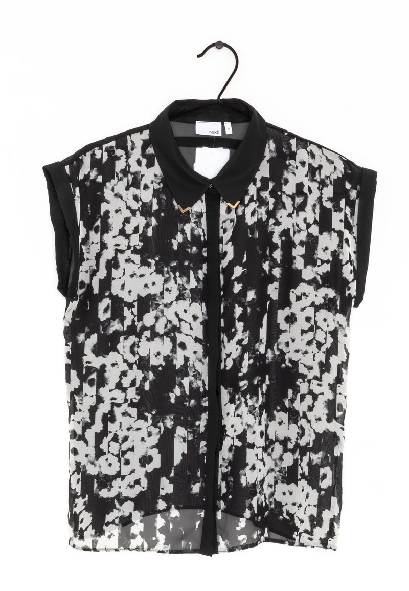 Blouse à manches courtes imprimé floral noir et blanc avec col noir et pointes de col dorées suspendue à un cintre noir.