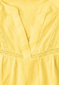 Vêtement jaune avec encolure en V et délicats détails de dentelle le long de l'encolure et de la taille.