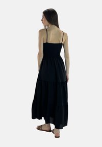 Sort maxi-kjole med tynde stropper, smocket bodice og tiered skørt design. Fremstillet af letvægtsstof med en glat tekstur.