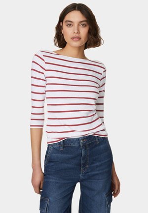Dame langærmet stribet top i hvid med røde striber, med bådhals og let rynkede sider. Kombineret med blå denimjeans.