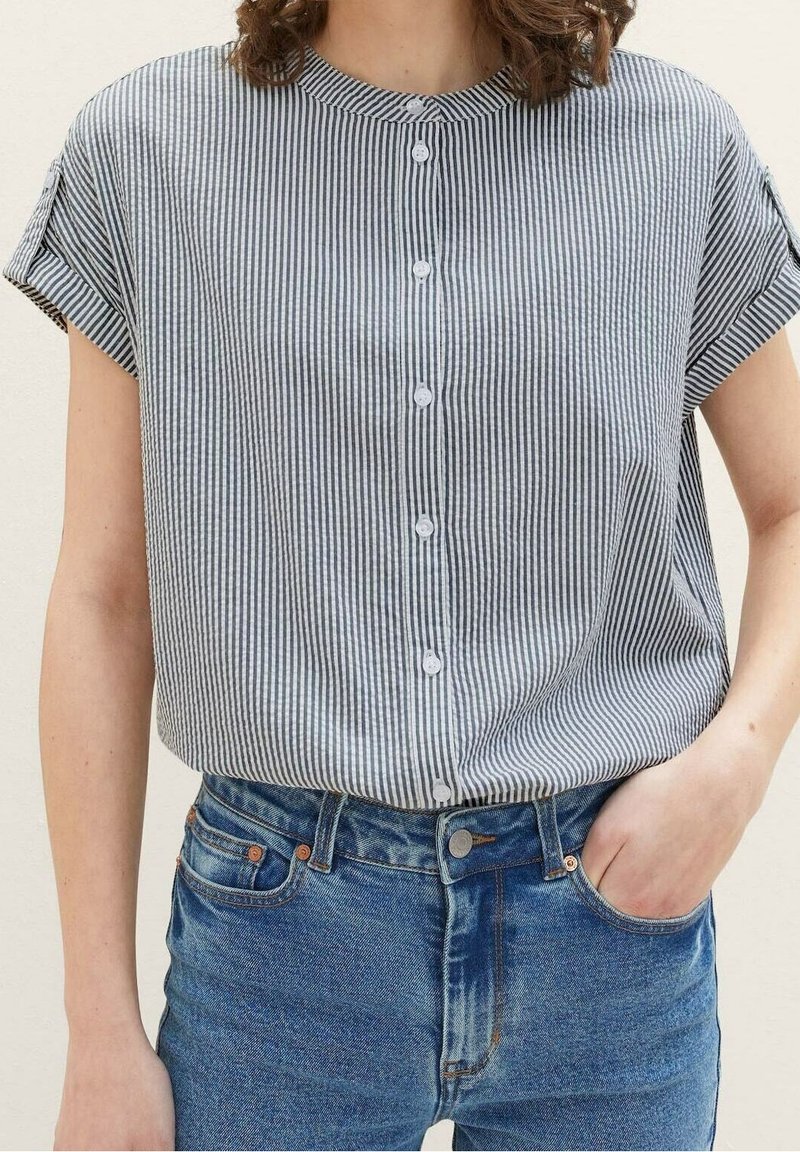 Båndet skjorte i marineblå og hvid, kortærmet, uden krave, blødt stof med en ustruktureret pasform, båret med blå jeans.