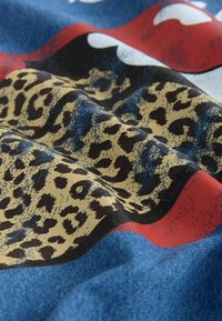 Denim fabric featuring bold red lips and a leopard print pattern on a blue background. Smooth texture with varying shades and contrasts.