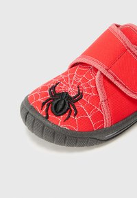 Chaussure en tissu rouge avec broderie de spider noire et motif de toile. Fermeture à bande Velcro et semelle en caoutchouc avec grip texturé.