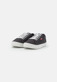 Zapatillas de lona negras con cordones blancos, puntera redonda y suela de goma blanca. Presentan un pequeño logotipo rojo en el panel lateral.