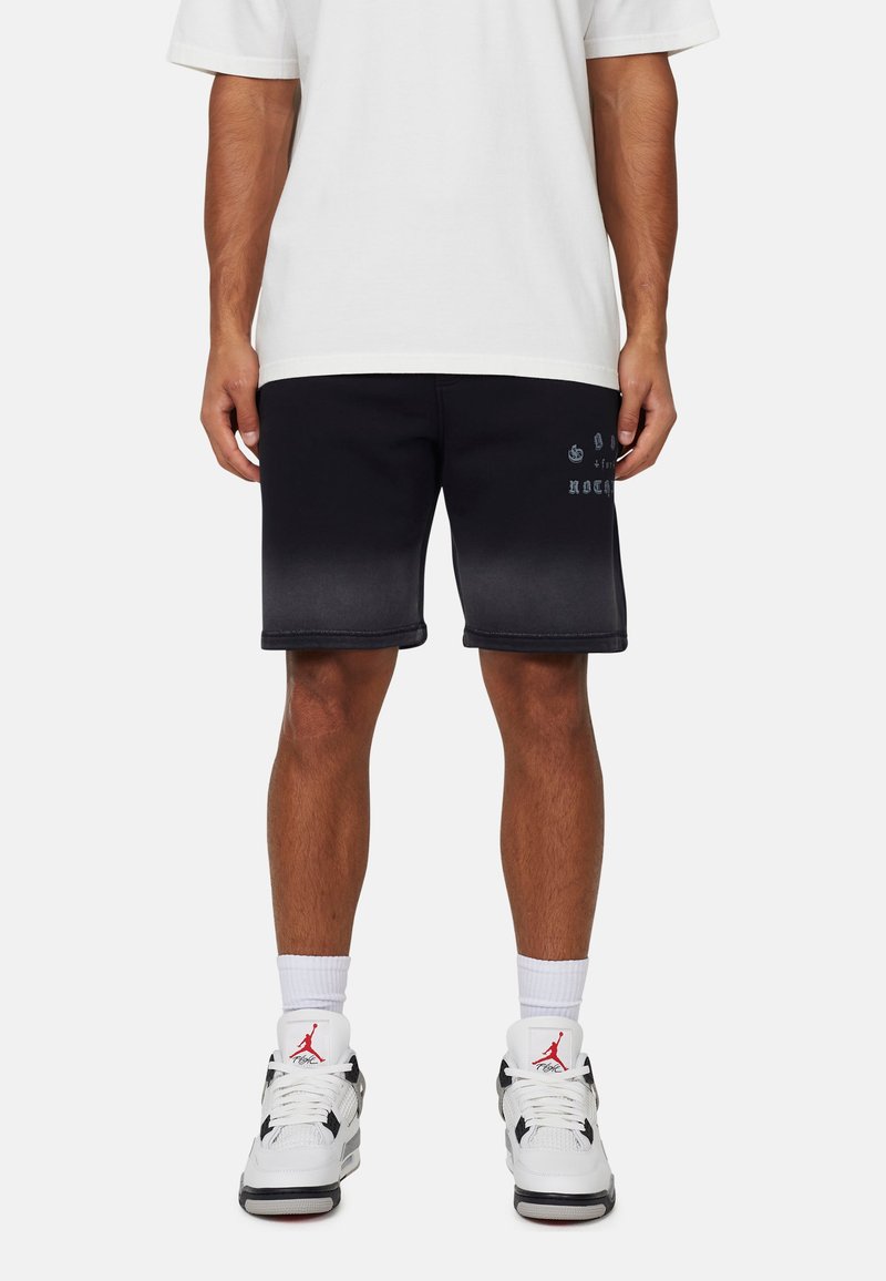 Pantaloni corti neri con una sfumatura al grigio, dotati di un testo grafico sottile sulla gamba. Indossati con calze bianche e scarpe sportive bianche e nere.