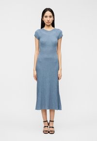 Μπλε ριμπ πλεκτό φόρεμα με κοντά μανίκια, εφαρμοστό κορσάζ και φαρδύ τελείωμα. Συνδυάζεται με μαύρα πέδιλα με λουράκια. Λεία υφή.