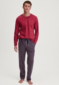 Rode lange mouwen top gecombineerd met marineblauwe gestreepte pyjamabroek met dunne witte en rode lijnen, elastische tailleband en zijzakken.