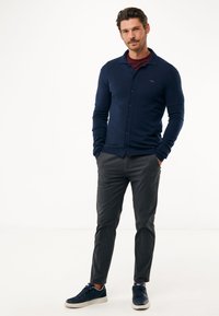 Námořnický svetr s knoflíkovou přední částí, ribovanými manžetami a slim fit střihem, v kombinaci s tmavě šedými kalhotami a námořnickými teniskami.