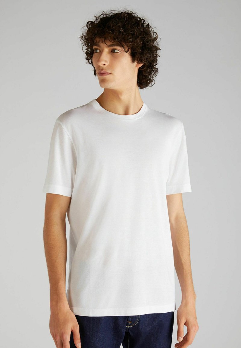 T-shirt bianca in cotone con scollo rotondo, maniche corte e taglio dritto, esposta su uno sfondo neutro.