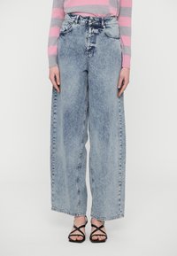 Light blue wide-leg denim jeans with a faded finish, high waist, five pockets, and a button closure. Worn with black strappy sandals.