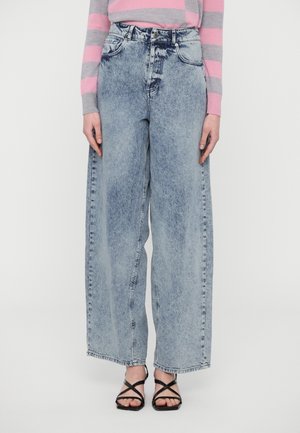 Lyseblå vide denimjeans med falmet finish, høy midje, fem lommer og knappelukking. Brukt med svarte sandaler med stropper.