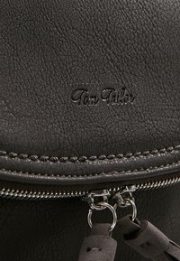 Borsa in pelle grigia scura con superficie testurizzata, chiusura con zip metallica e nome del marchio "Tom Tailor" in rilievo sul davanti.