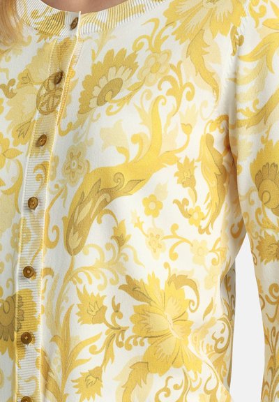 Cardigan blanc avec motif floral et feuillagé jaune, doté de boutons marron sur le devant et d'un col côtelé.