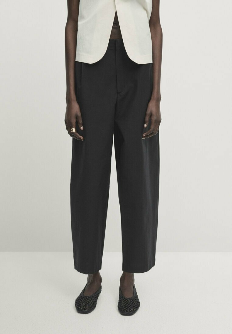 Czarne spodnie szerokie wykonane z lekkiego materiału, o prostym kroju, wysokim stanie i delikatnym drapowaniu. W połączeniu z plecionymi czarnymi butami.