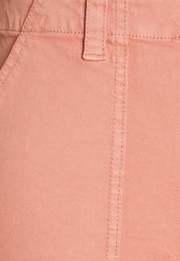 Tessuto corallo chiaro con una texture liscia, caratterizzato da cuciture angolari e una vita cucita. Primo piano del motivo della trama del denim.