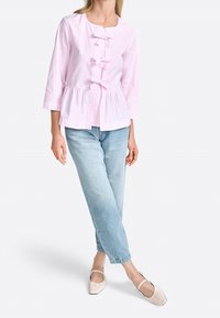 Bledě růžová pruhovaná blůza s peplum spodním lemováním, která má tři mašle na přední části, spárovaná se světle modrými džíny a béžovými balerínami.