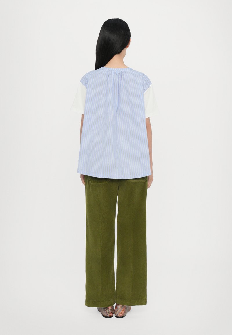 Lichtblauw en wit gestreepte blouse met een losse pasvorm, gecombineerd met olijfgroene wijde corduroy broek. Gelaagd textiel en ontspannen silhouet.