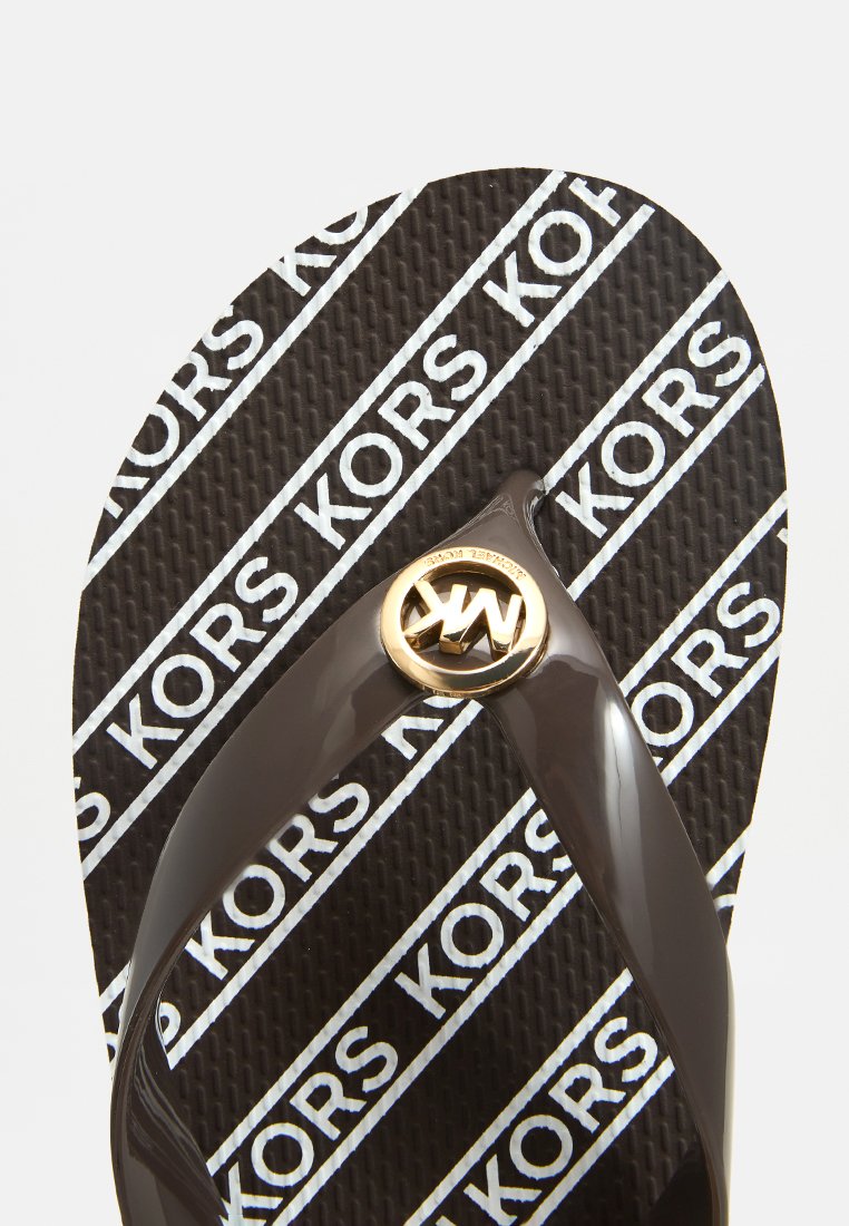 Tongs en caoutchouc marron avec une lanière texturée. La semelle intérieure présente un fond noir avec des motifs répétitifs du logo blanc "KORS". Détail en matériel doré.