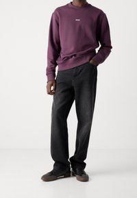 Fialová mikina s logem "BOSS", doplněná volnými černými džínami a černými teniskami s hnědými akcenty. Hladká tkanina a uvolněný střih.