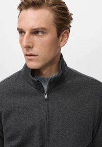 Maglione grigio con zip e collo alto, realizzato in tessuto morbido, con una texture liscia e dettagli di cucitura discreti lungo le spalle.