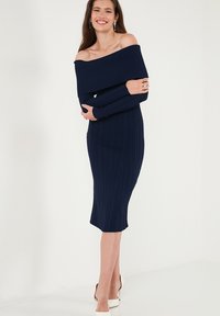 Abito navy a coste con spalle scoperte, maniche lunghe, silhouette aderente e orlo al ginocchio. Tessuto liscio e sottili righe verticali.