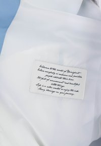 Tissu blanc avec un patch rectangulaire cousu présentant un texte en cursive noire sur la vie, l'amusement et l'accueil des gens dans un message positif.