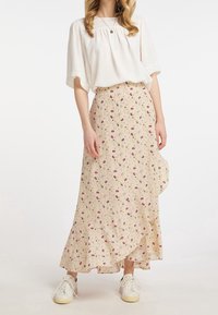 Gonna maxi floreale in beige chiaro con motivi rosa e verdi, caratterizzata da un orlo arricciato e abbinata a sneaker bianche e a una maglietta bianca ampia.