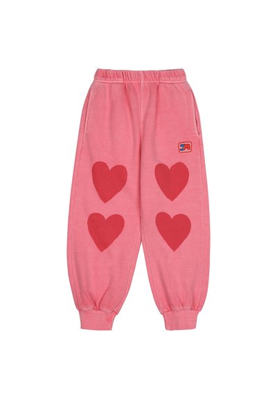 Rózsaszín melegítőnadrág, elől három nagy piros szív applikációval, rugalmas derékkal, mandzsettákkal és oldalsó zsebekkel. Párna logó a csípőn.