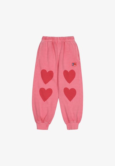 Rózsaszín melegítőnadrág, elől három nagy piros szív applikációval, rugalmas derékkal, mandzsettákkal és oldalsó zsebekkel. Párna logó a csípőn.