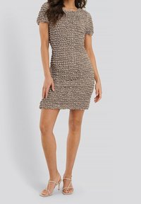 Korte mouwen, getailleerde jurk in taupe met gestructureerde, geplooide stof. Soepele halslijn, knielange zoom, gecombineerd met nude, gespen hakken.