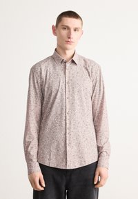 Camicia a bottoni di colore rosa chiaro con una stampa geometrica sparsa in blu navy e bianco. Maniche lunghe, collo classico e orlo curvo.