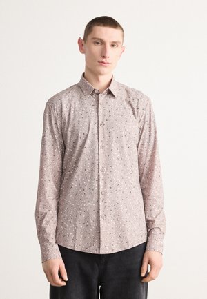 Camisa de botón en rosa claro con un estampado geométrico disperso en azul marino y blanco. Mangas largas, cuello clásico y un dobladillo curvado.