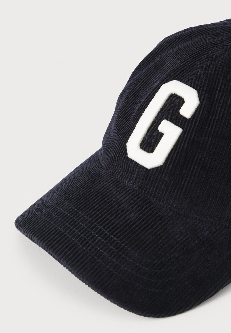Granatowa czapka z kordurowego materiału z wygięnym daszkiem i białym haftowanym napisem "G" z przodu. Teksturowana powierzchnia nadaje jej unikalny wygląd.