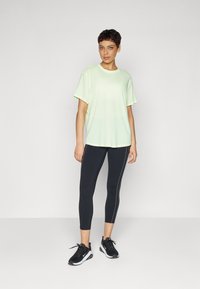 Lysegrønn t-skjorte med korte ermer, kombinert med svarte leggings med hvite sidestreker, og svarte joggesko.