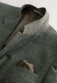 Blazer gris à carreaux avec col relevé, doublure en satin marron et un mouchoir de poche marron assorti.