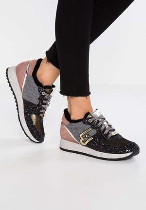 Osoba ubrana w czarne spodnie do połowy łydki oraz czarne, szare, różowe i złote połyskujące trampki z futrzanym wykończeniem i grubymi białymi podeszwami.