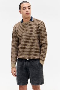 Pull marron à motifs avec un col marine, associé à un short en velours côtelé noir, doté de poches latérales et à coupe décontractée.