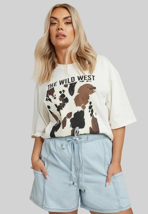 White oversized t-shirt with "THE WILD WEST" text and brown animal print, paired with light blue drawstring shorts featuring front pockets.