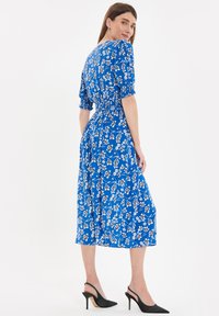 Vestido azul floral con mangas cortas y abullonadas, cintura ajustada y largo midi. Presenta una textura suave y patrones de flores blancas.