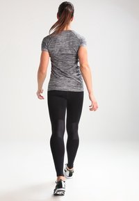 Conjunto atlético que incluye una camiseta de manga corta en gris jaspeado y leggings negros. Los leggings tienen una sutil textura y un diseño ajustado.