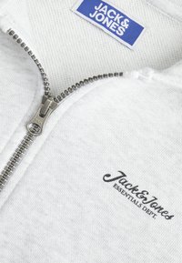 Felpa zip grigia chiara con zipper in metallo. Presenta un'etichetta tessuta al collo e la scritta "Jack & Jones" ricamata in nero sul davanti.