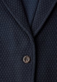 Veste en tricot texturée bleu marine foncé avec un seul bouton noir gravé du mot "STREETONE" à la fermeture avant.