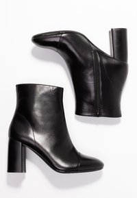 Bottines noires en cuir avec une texture lisse, bout arrondi et talon carré. Dotées d'une fermeture éclair sur le côté.