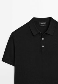 Polo shirt in cotone nero con colletto a ribaltina, pattina con tre bottoni e maniche corte. Texture liscia, design minimalista.