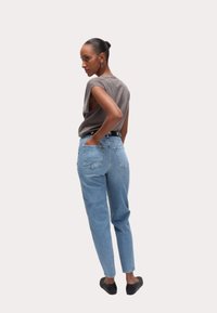 Graues ärmelloses Oberteil, hellblaue High-Waist-Jeans, Rückansicht. Die Jeans verfügen über zwei Gesäßtaschen und eine figurbetonte Silhouette. Schwarze Slipper.