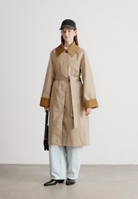 Beež värvi trikood mantlikrae ja mansettidega, vööga talje juures seotud. Kandmiseks helesiniste laia säärega pükstega ja mustade kontsakingadega.