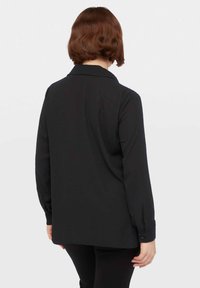 Camicia nera a maniche lunghe con vestibilità ampia, dotata di colletto e sottili motivi a pois. Texture liscia e polsini con bottoni sulle maniche.
