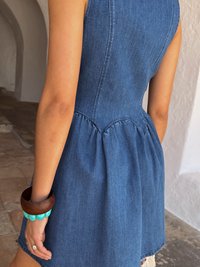 Traper haljina s uskim korzetom i peplum detaljem, koja ima bezrukavi dizajn. Dodaci uključuju drveni narukvicu i narukvicu u tirkiznoj boji.