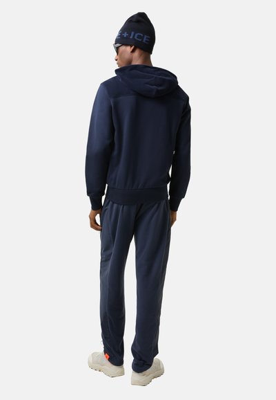 Navy blue hoodie and joggers set made of soft fabric, featuring a hood and ribbed cuffs, paired with light-colored sporty shoes.