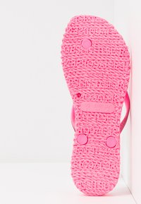 Vaaleanpunainen flip-flop-pohja, jossa on teksturoitu kuvio, kokomerkinnät (US 7, EUR 37, UK 4) ja pyöreät napit säädettävää istuvuutta varten.